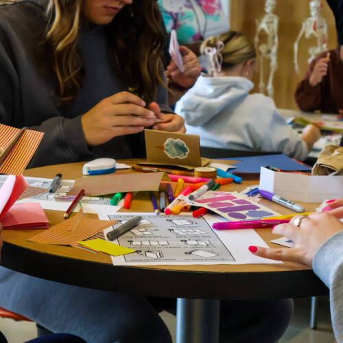 Students craft with colorful crafting supplies on a table (zine workshop at GV).